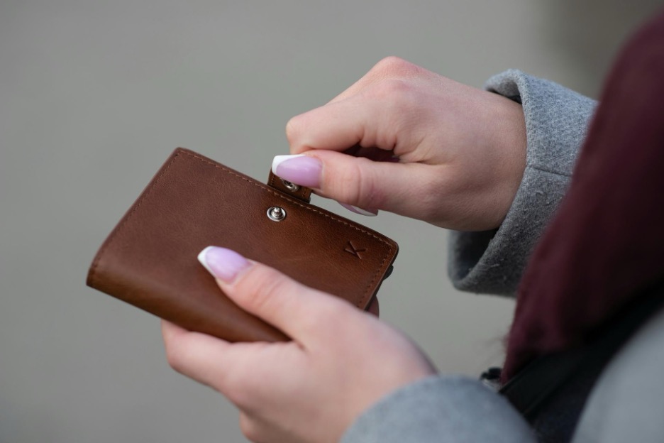 Close-up of a woman’s hands opening a brown leather wallet.
