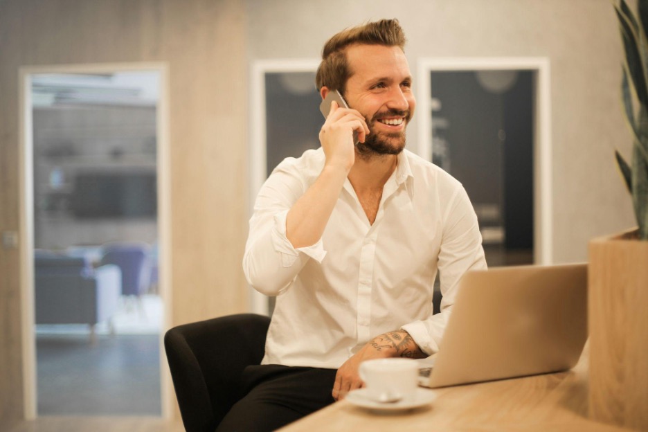 A man in a cafe holding a cell phone to his ear and smiling.