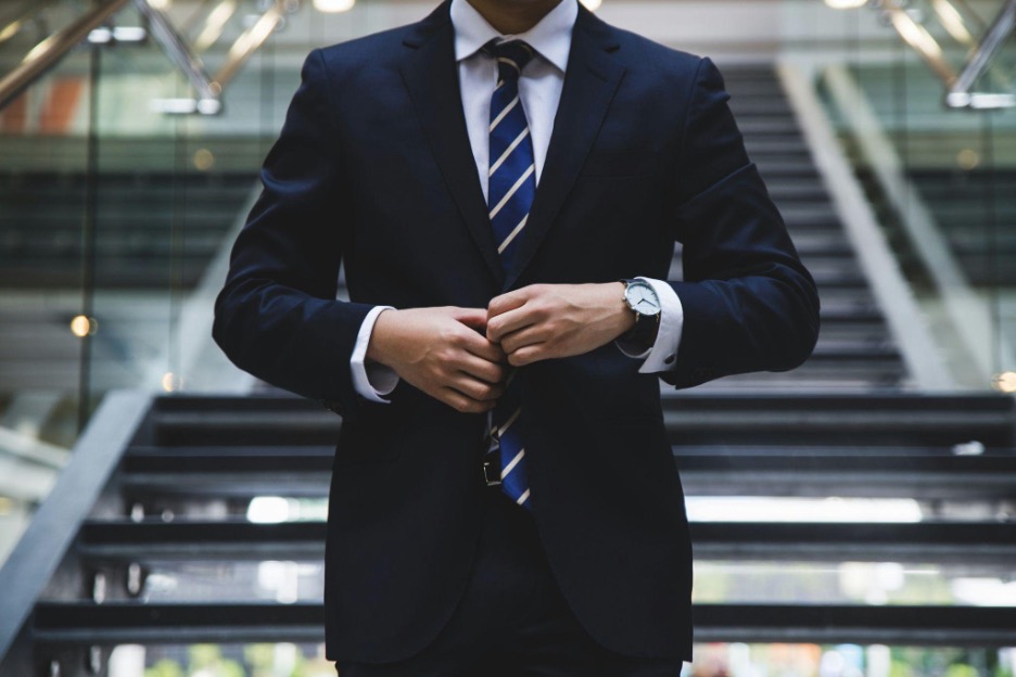 Torso of a man in a suit walking down the stairs and buttoning his jacket.