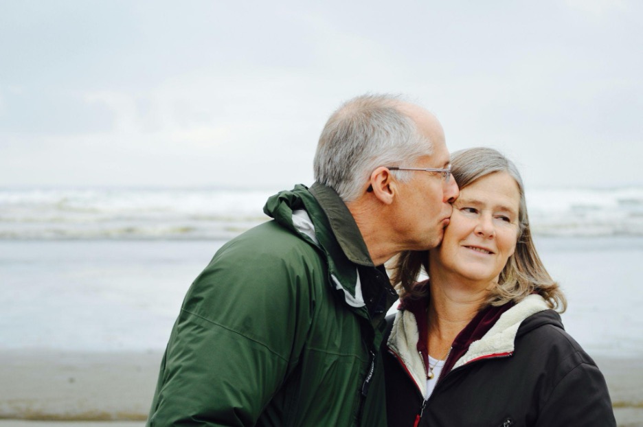 Man kissing woman on the cheek with a beach in the background.