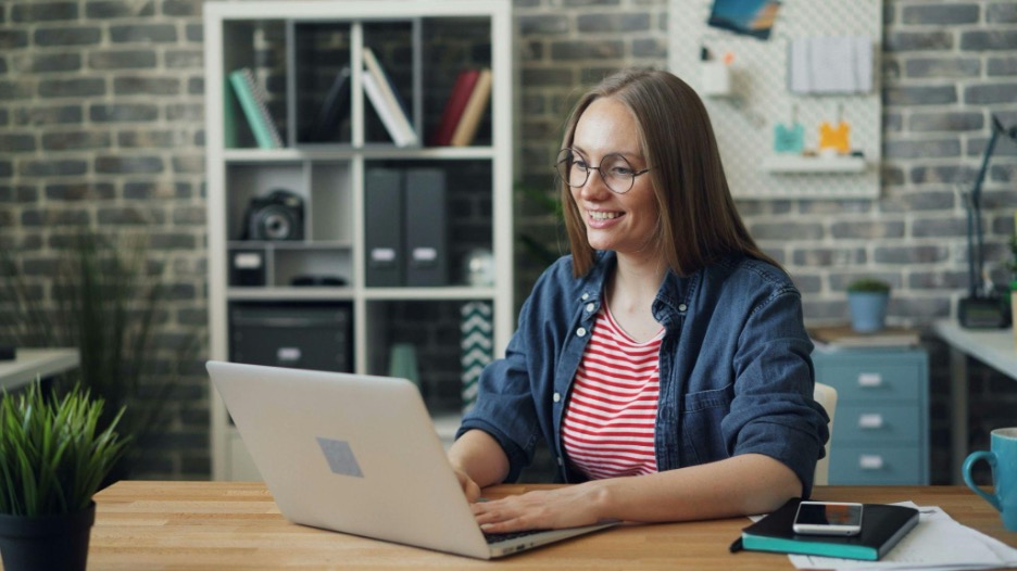 Woman sitting behind a wooden desk looking at a laptop with her hands on the keyboard.
