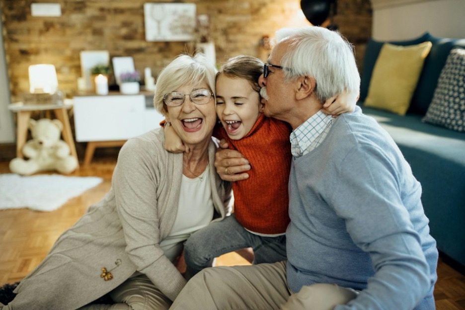 Two grandparents smile and hug their grandchild between them.