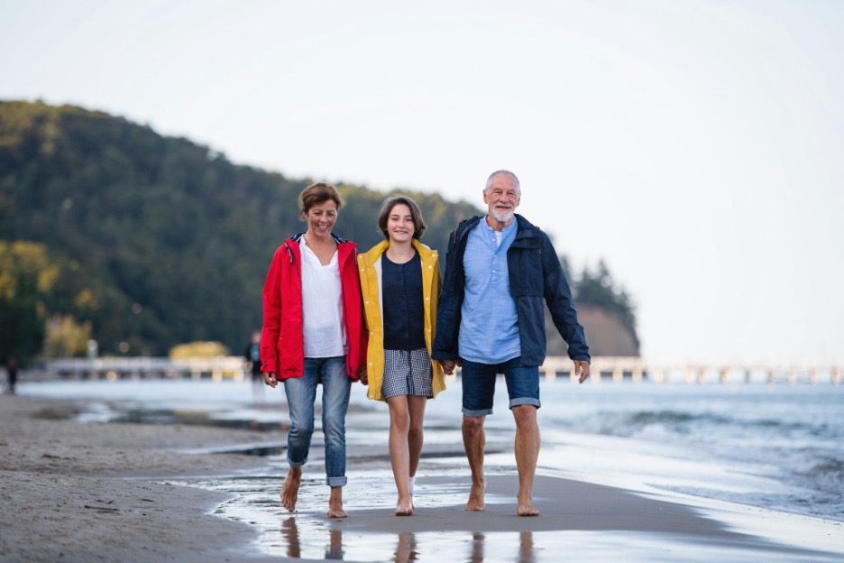 Smiling older couple walking barefoot on a beach with a young girl between them.